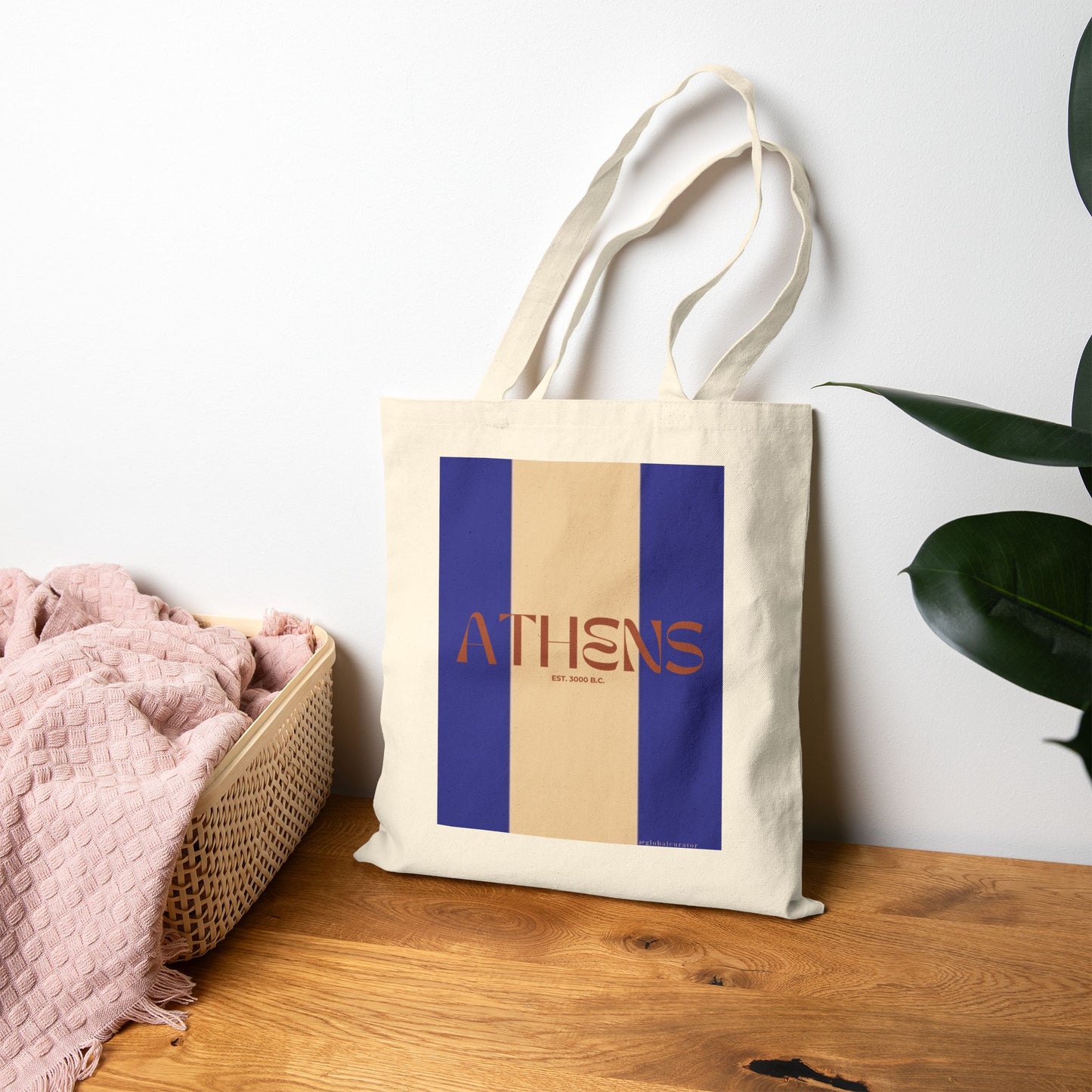 Tote bag with 'Athens' design on a wooden surface with a plant in the background