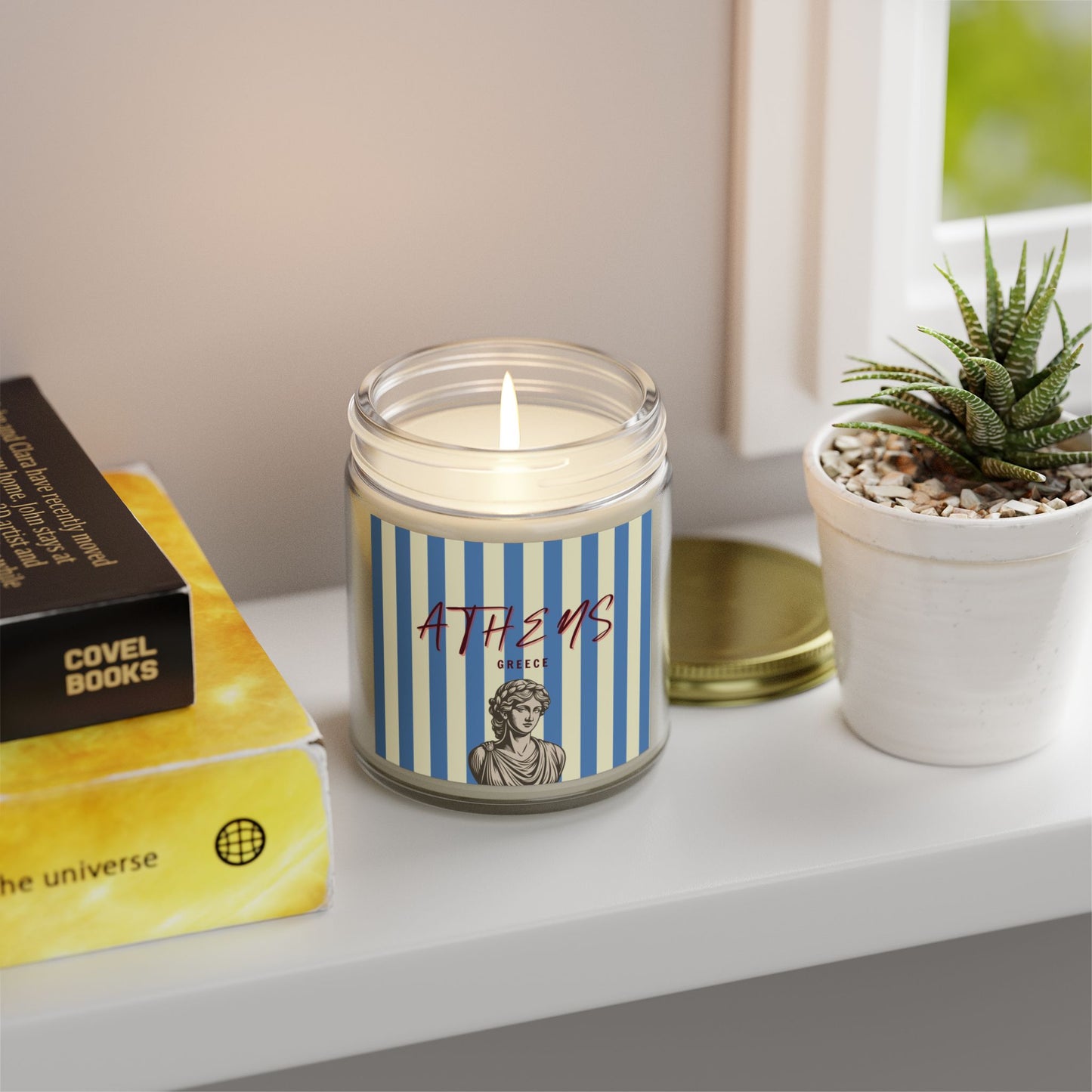 Candle with a striped label on a shelf next to books and a plant