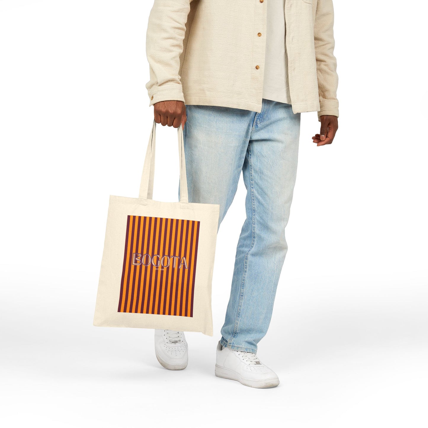 Person holding a tote bag with a striped pattern and visible brand name on a white background