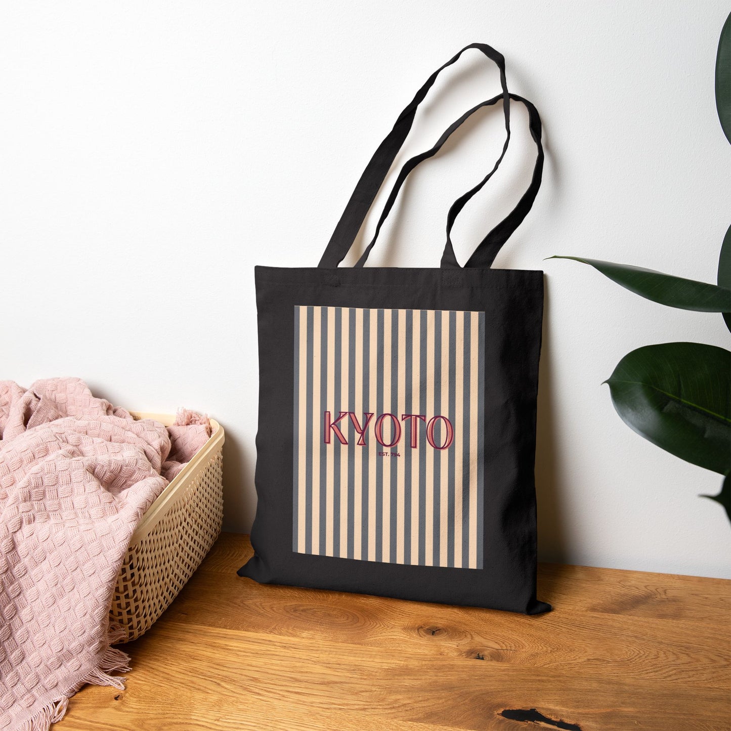 Black tote bag with 'KYOTO' text and striped design on a wooden surface.