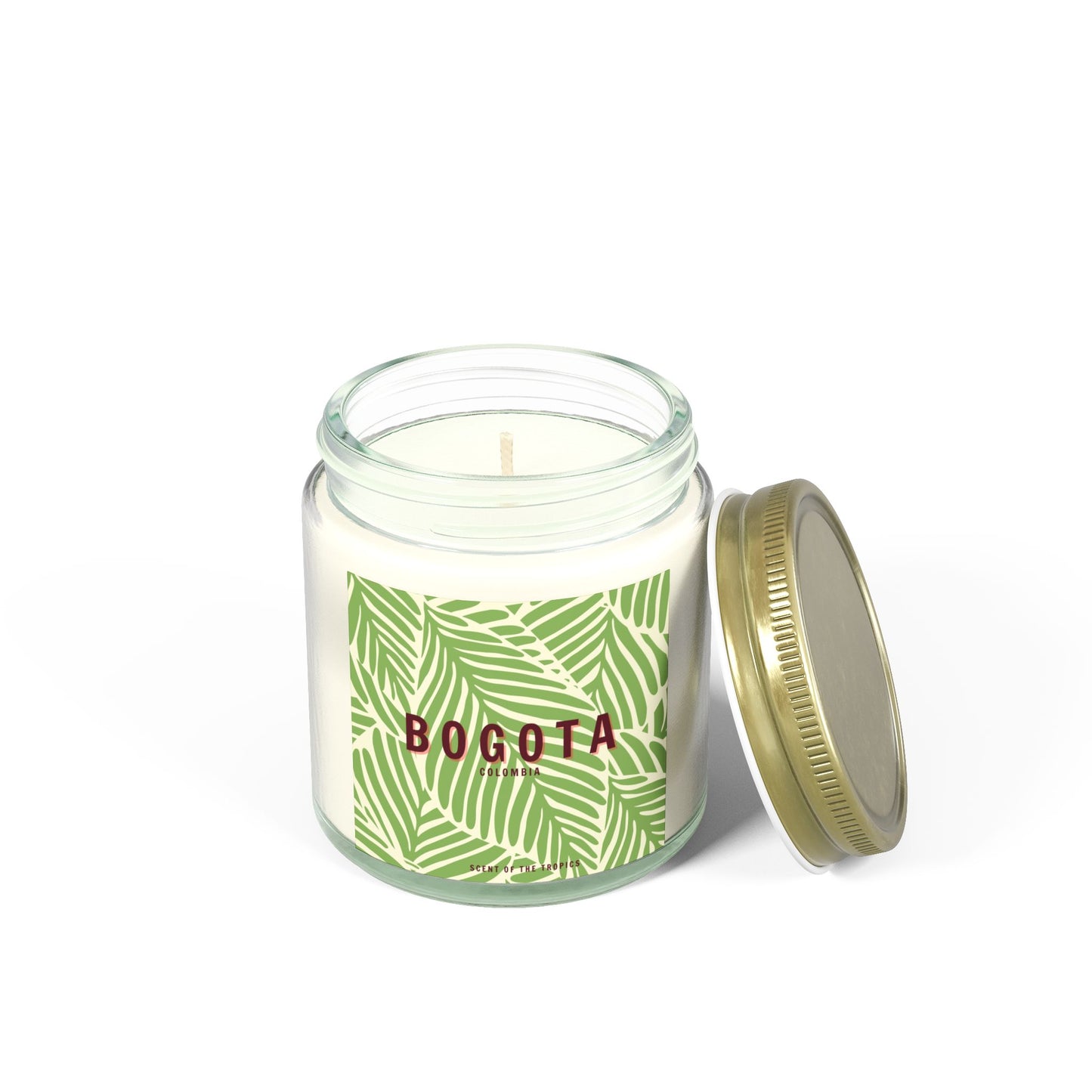 A glass candle vessel with a gold lid labeled 'BOGOTA' with a green leaf pattern.