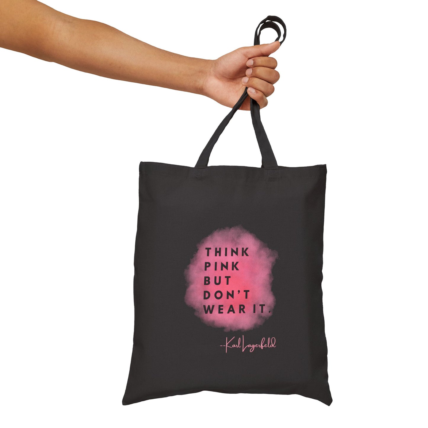 Black tote bag with pink design and text held by a hand on a white background