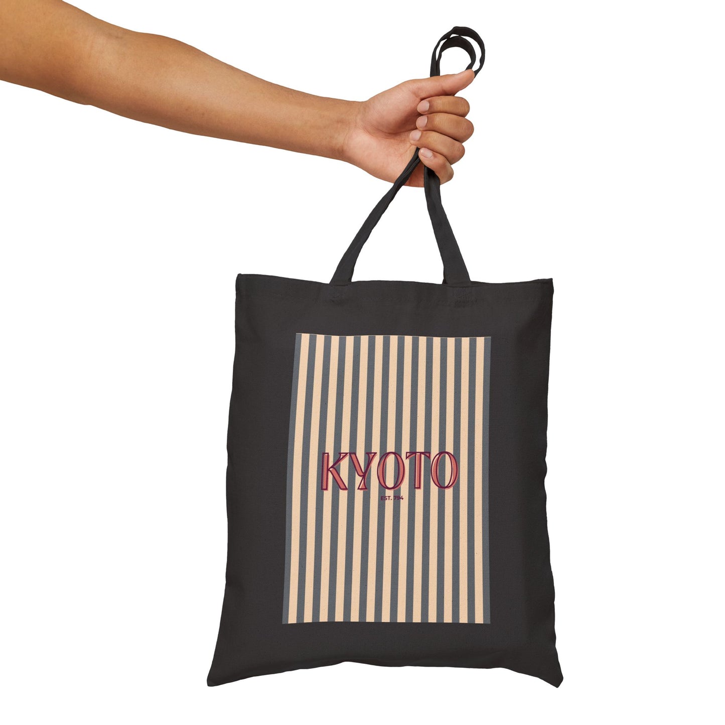 Black tote bag with 'KYOTO' text and striped pattern held by a hand on a white background