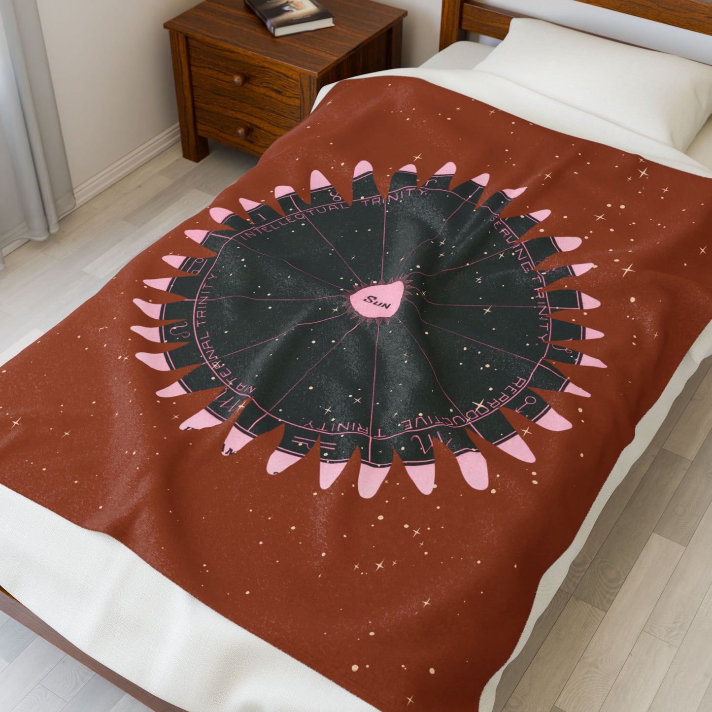Blanket with astrological design featuring pink and black elements on a bed in a bedroom.