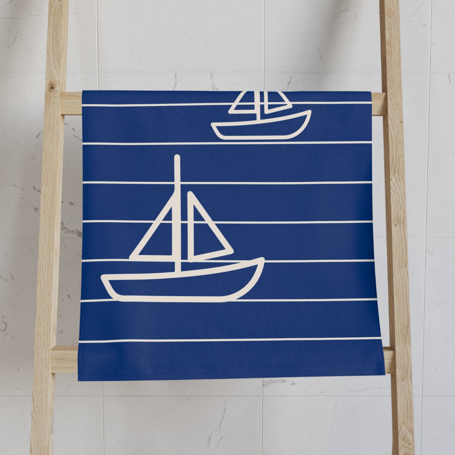 Navy blue towel with white sailboat designs on a wooden ladder against a white wall.