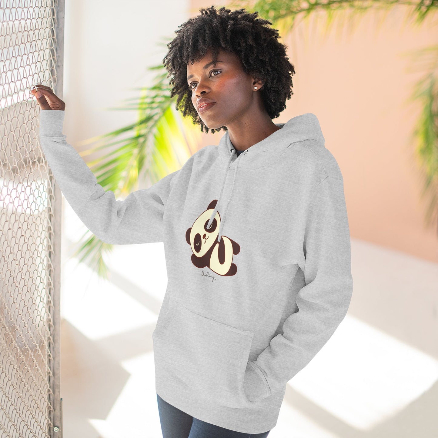 Person wearing a gray hoodie with a panda design, standing against a light background with plants.