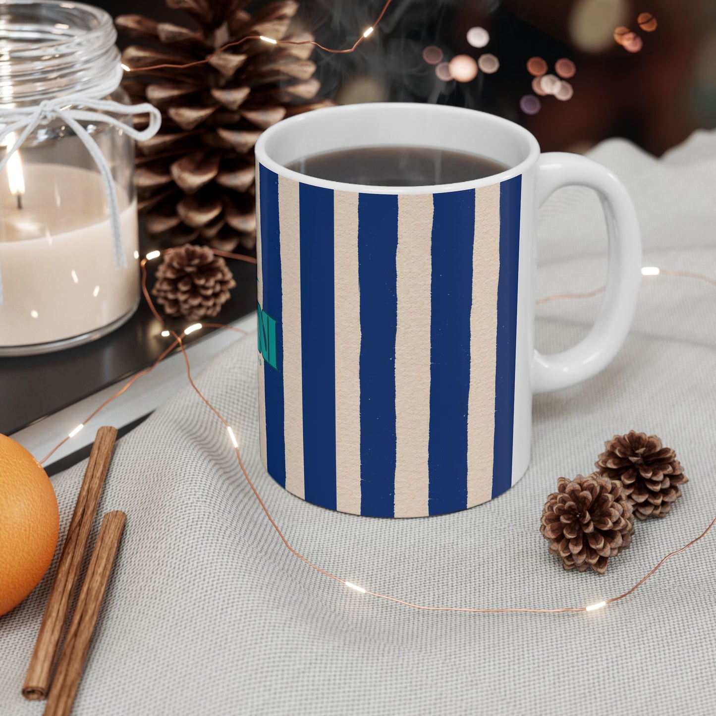 Striped mug with a warm beverage on a cozy setting with candles and pinecones.