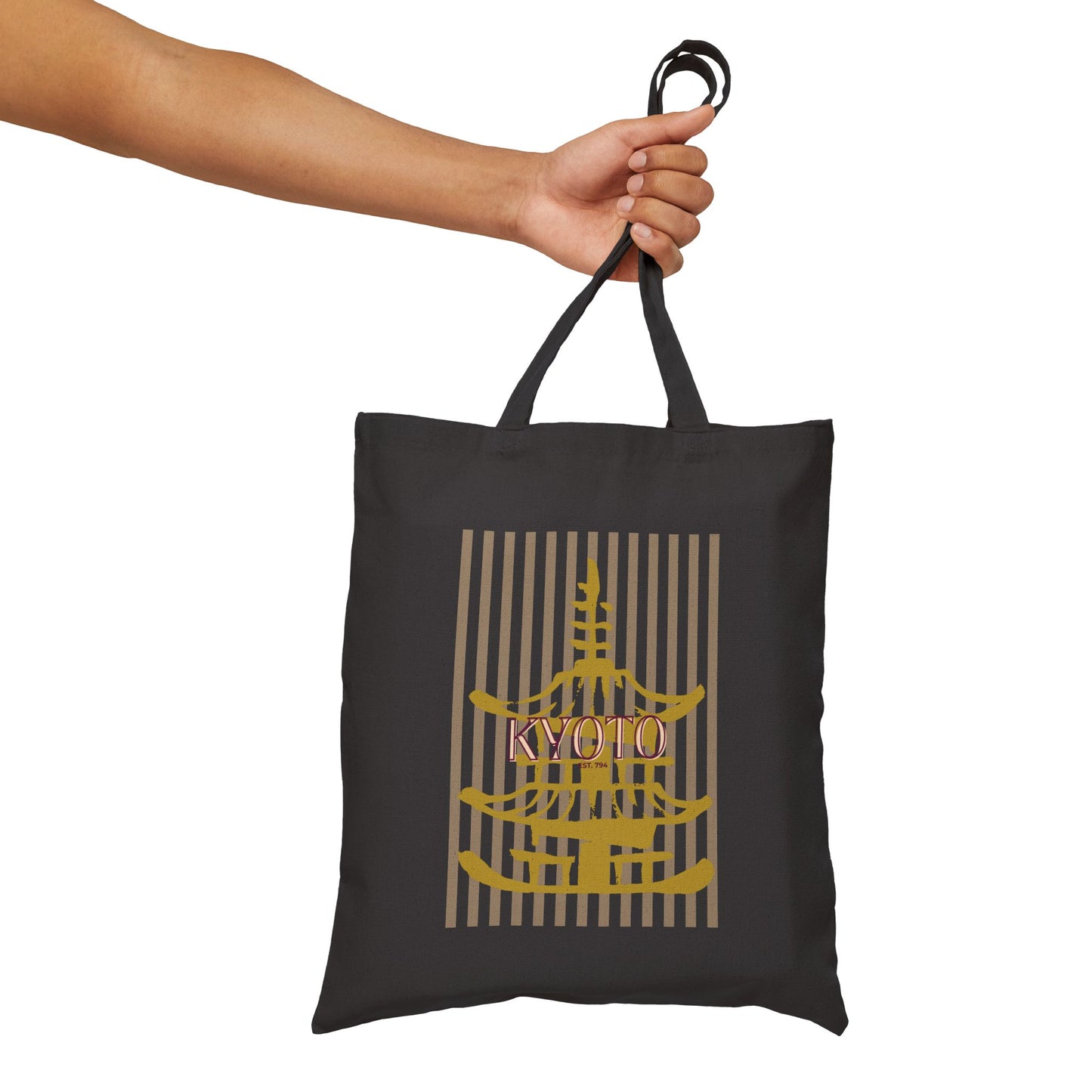 Black tote bag with gold and beige design held by a hand on a white background