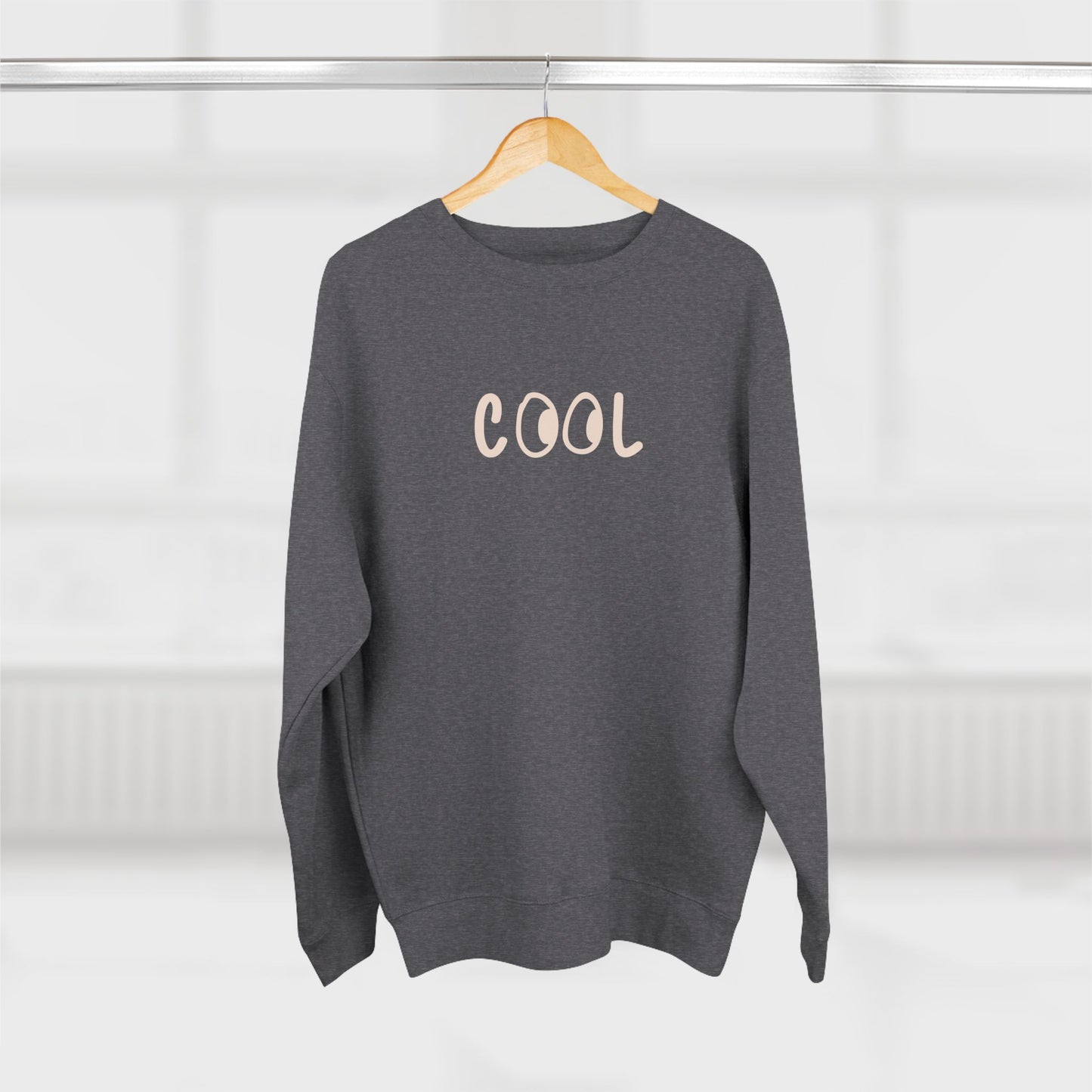 Gray sweatshirt with 'COOL' text on a wooden hanger against a white background