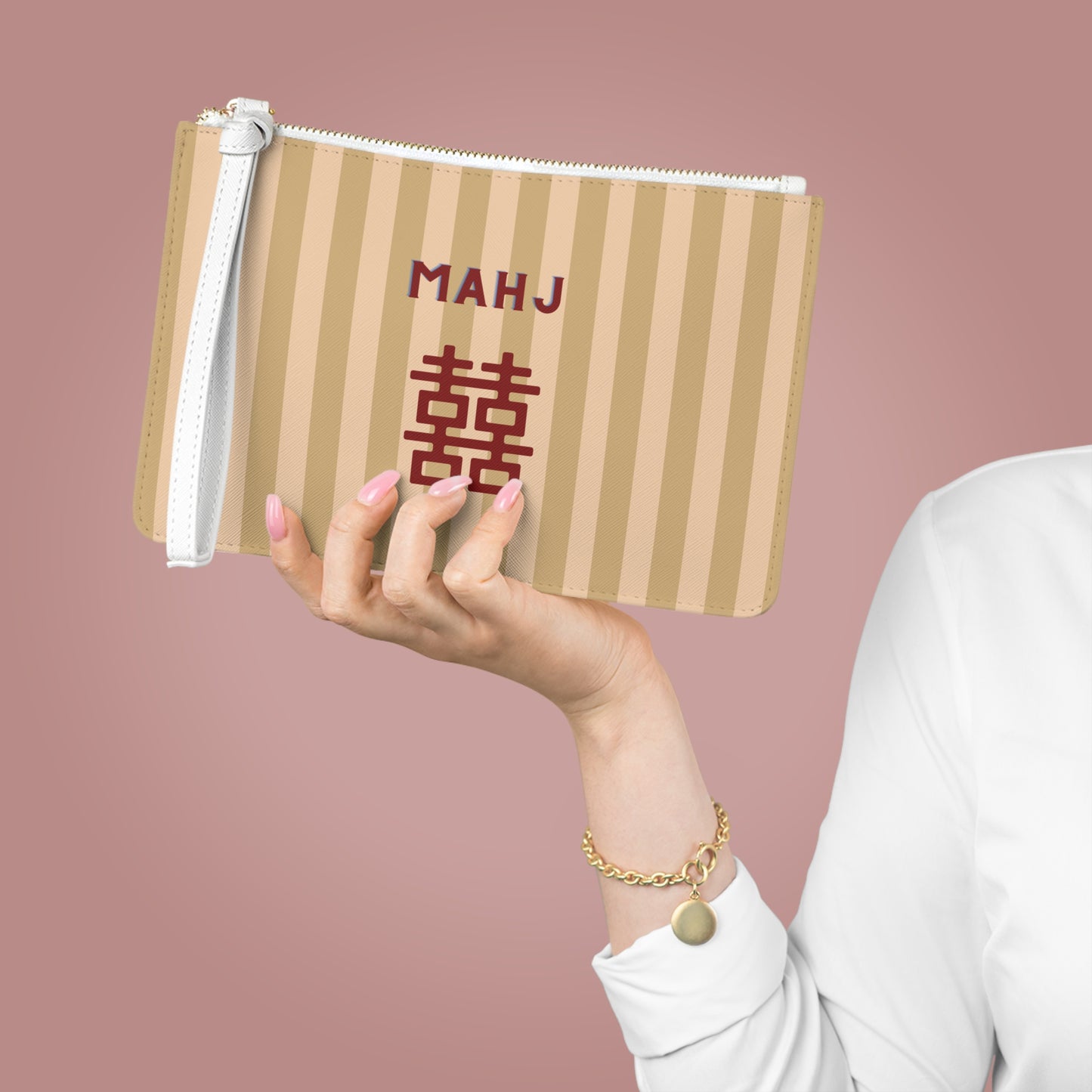 A person holds a beige and tan vertically striped zippered pouch with a white wrist strap. The pouch features the text 'MAHJ' in dark red above a large red double happiness symbol.
