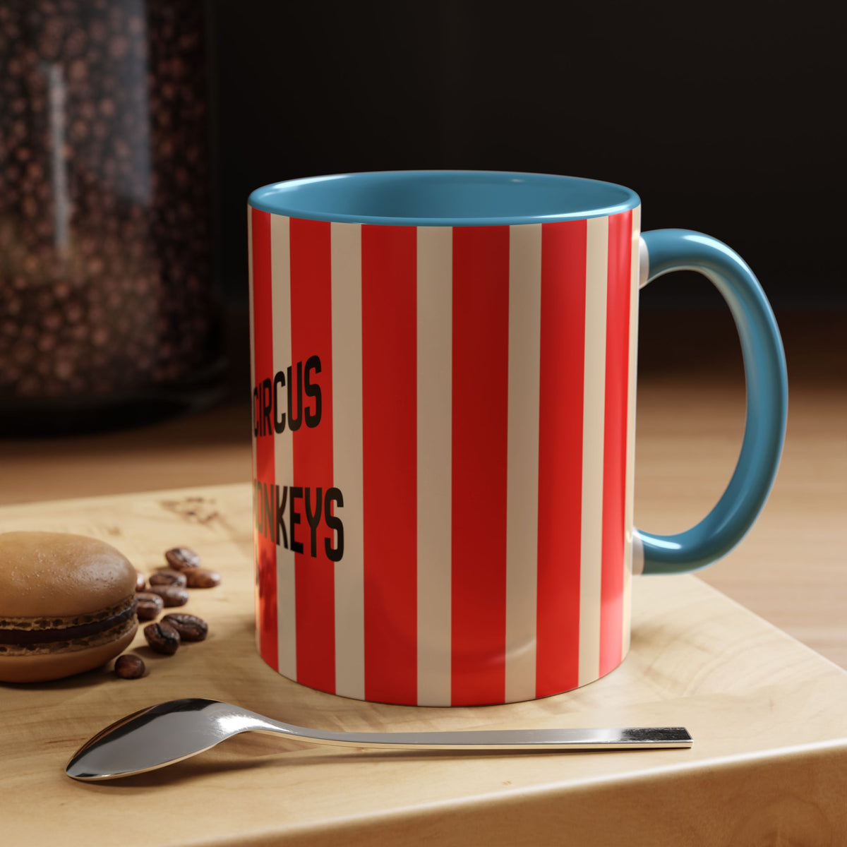 A ceramic coffee mug with red and white vertical stripes and a blue handle/interior, sitting on a wooden surface next to a spoon and coffee beans.