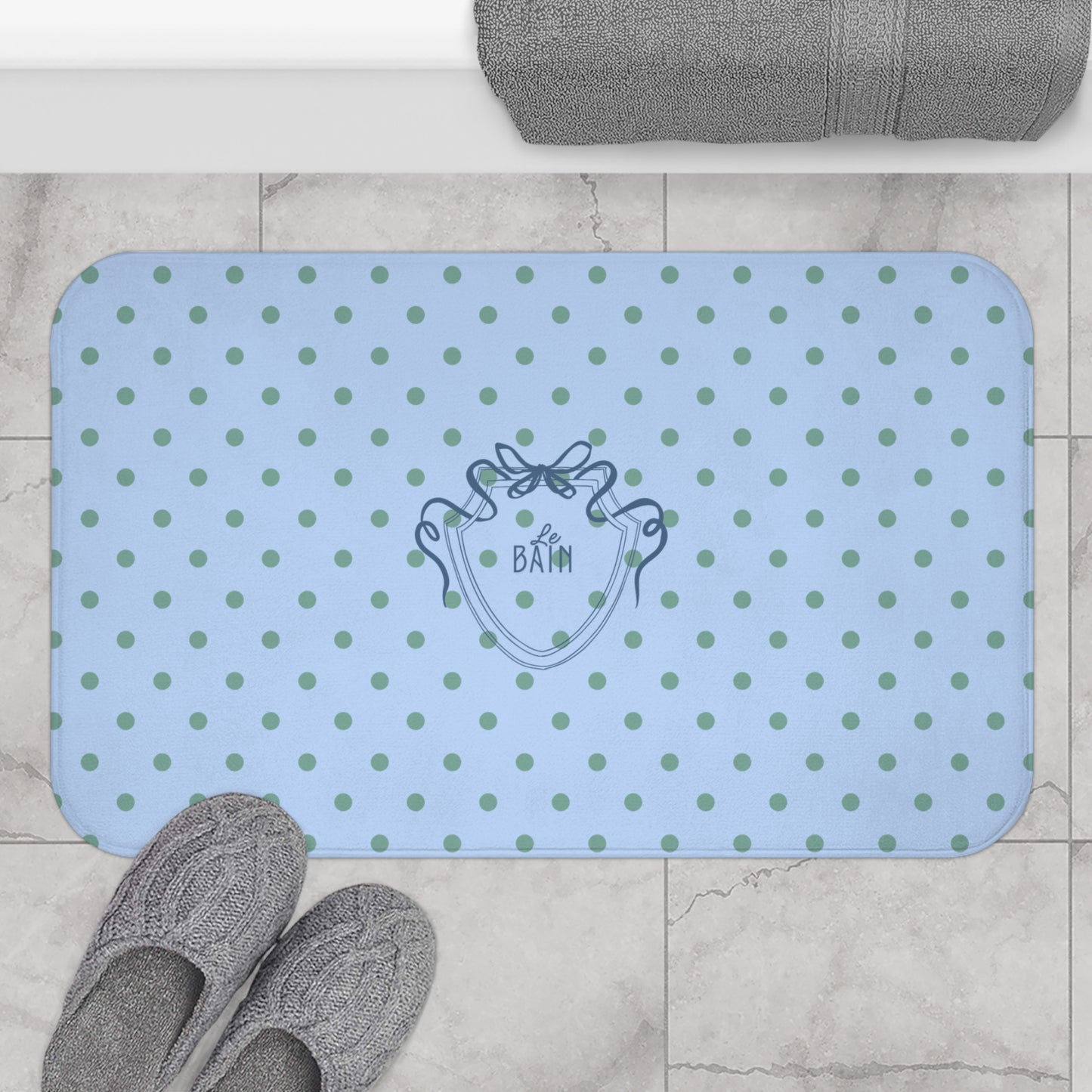 Blue polka dot bath mat with a brand logo on a tiled floor.