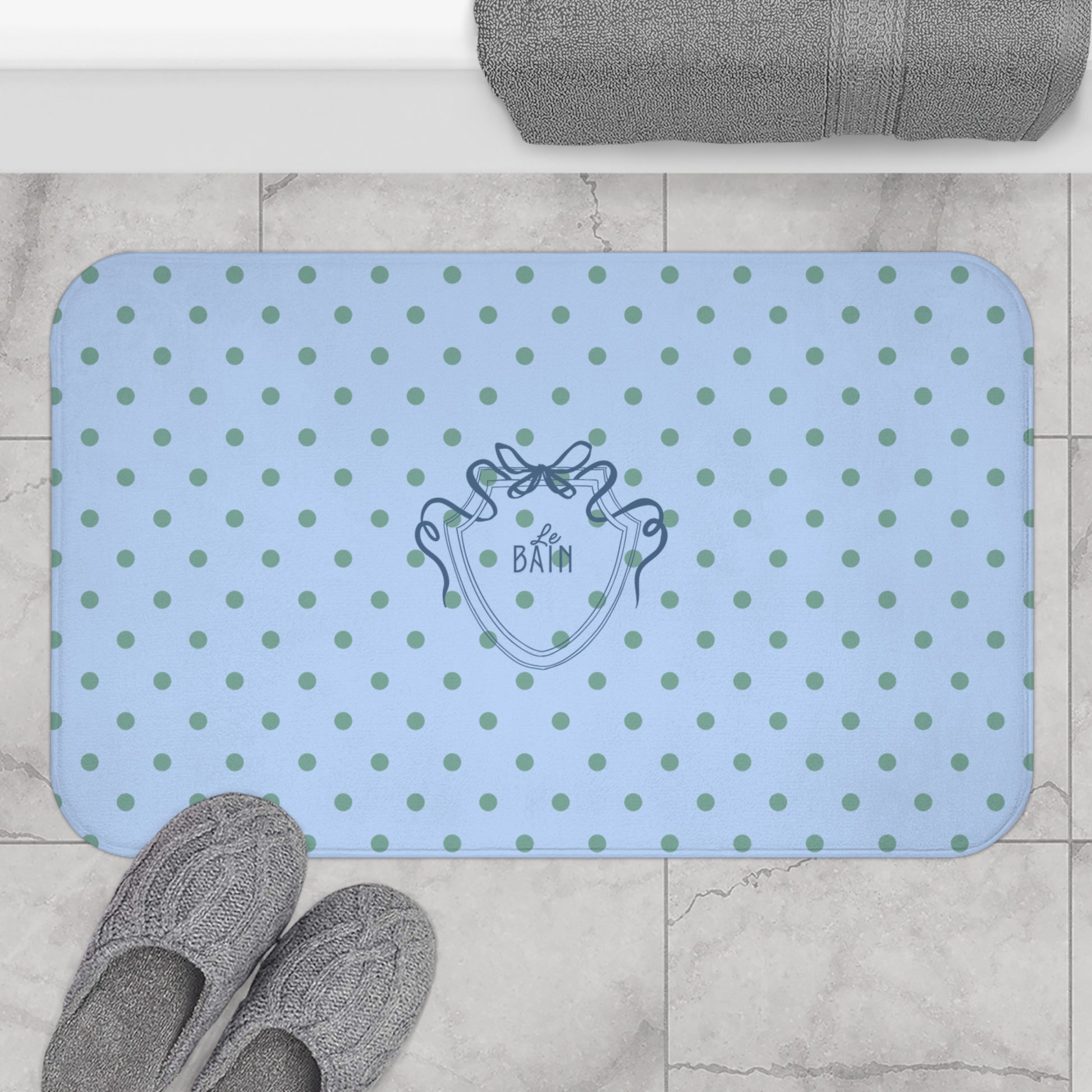 Blue polka dot bath mat with a brand logo on a tiled floor.