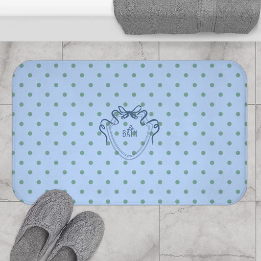 Blue polka dot bath mat with a brand logo on a tiled floor.