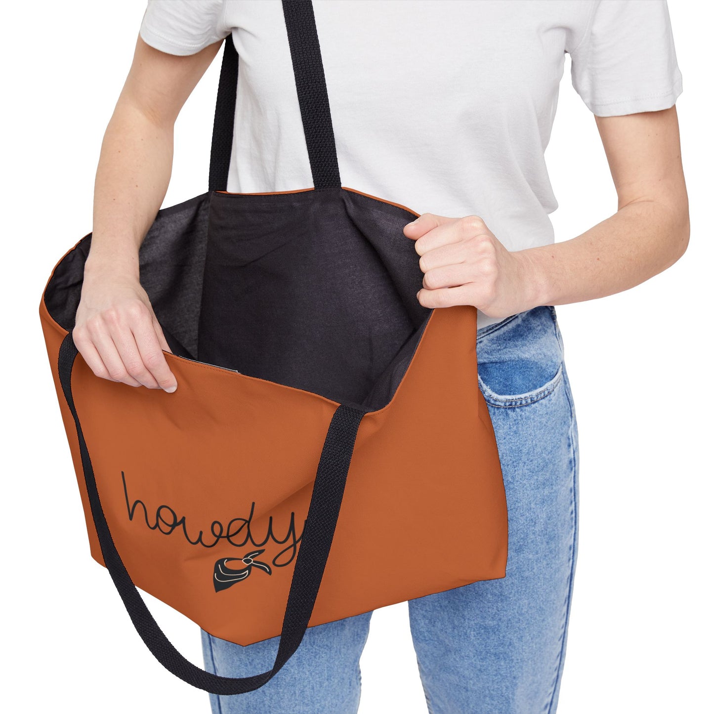 Person holding a brown and black tote bag with 'howdy' embroidery on a white background