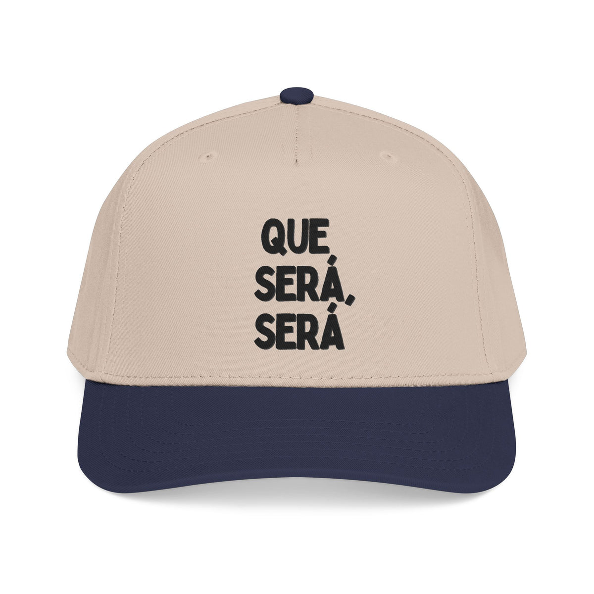 A structured baseball cap with a light beige crown and a dark navy blue visor, featuring the Spanish text 'QUE SERÁ, SERÁ' printed in black on the front panels.