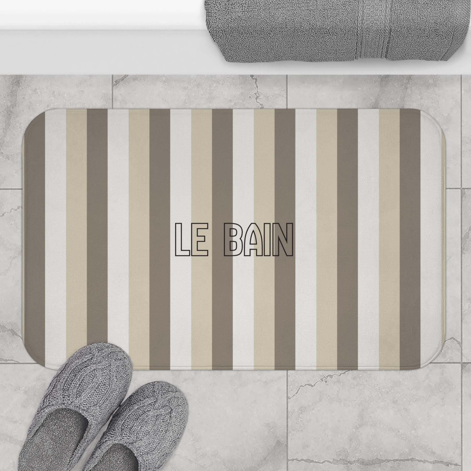 Striped bath mat with 'LE BAIN' text on a bathroom floor.