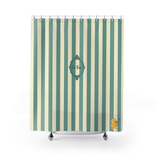 A shower curtain with vertical stripes in sage green and cream, featuring a central teal decorative frame with the monogram 'Le Bain and a small yellow rubber duck in the bottom right corner.