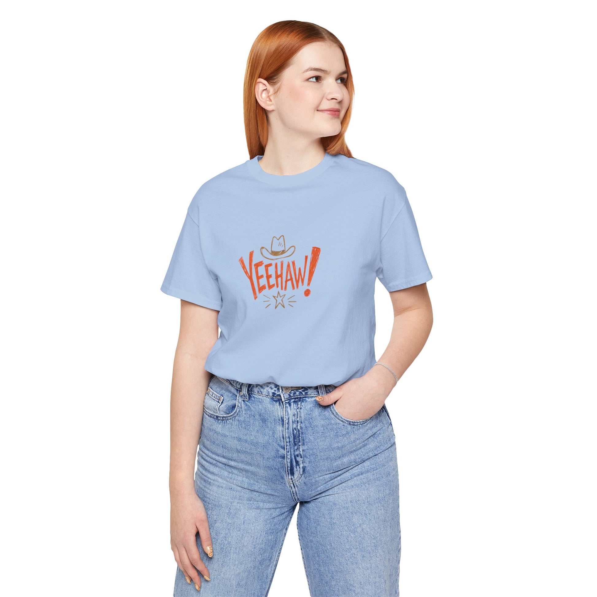 A woman with red hair wearing a light blue crewneck t-shirt with a red and white 'Veehaw!' graphic, paired with light wash blue jeans, against a plain white background.