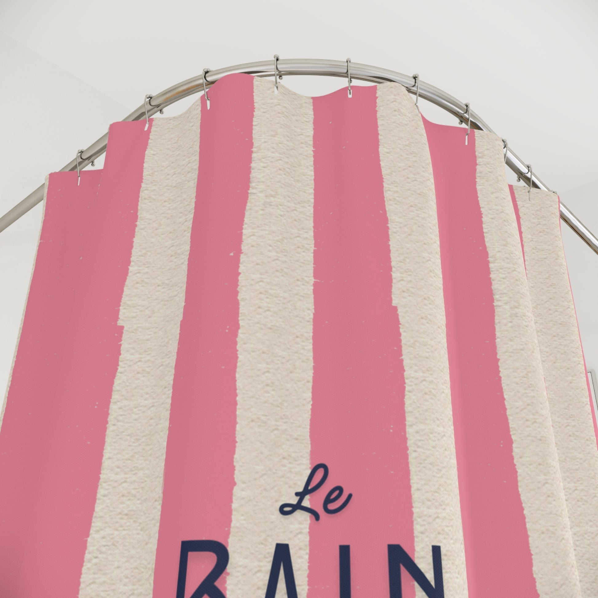 Pink and beige striped towel with 'Le Bain' text on a metal rack.