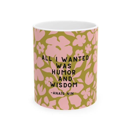 A white ceramic mug featuring a pink and olive green floral pattern with the quote 'ALL I WANTED WAS HUMOR AND WISDOM -ANAIS NIN' printed in black text.