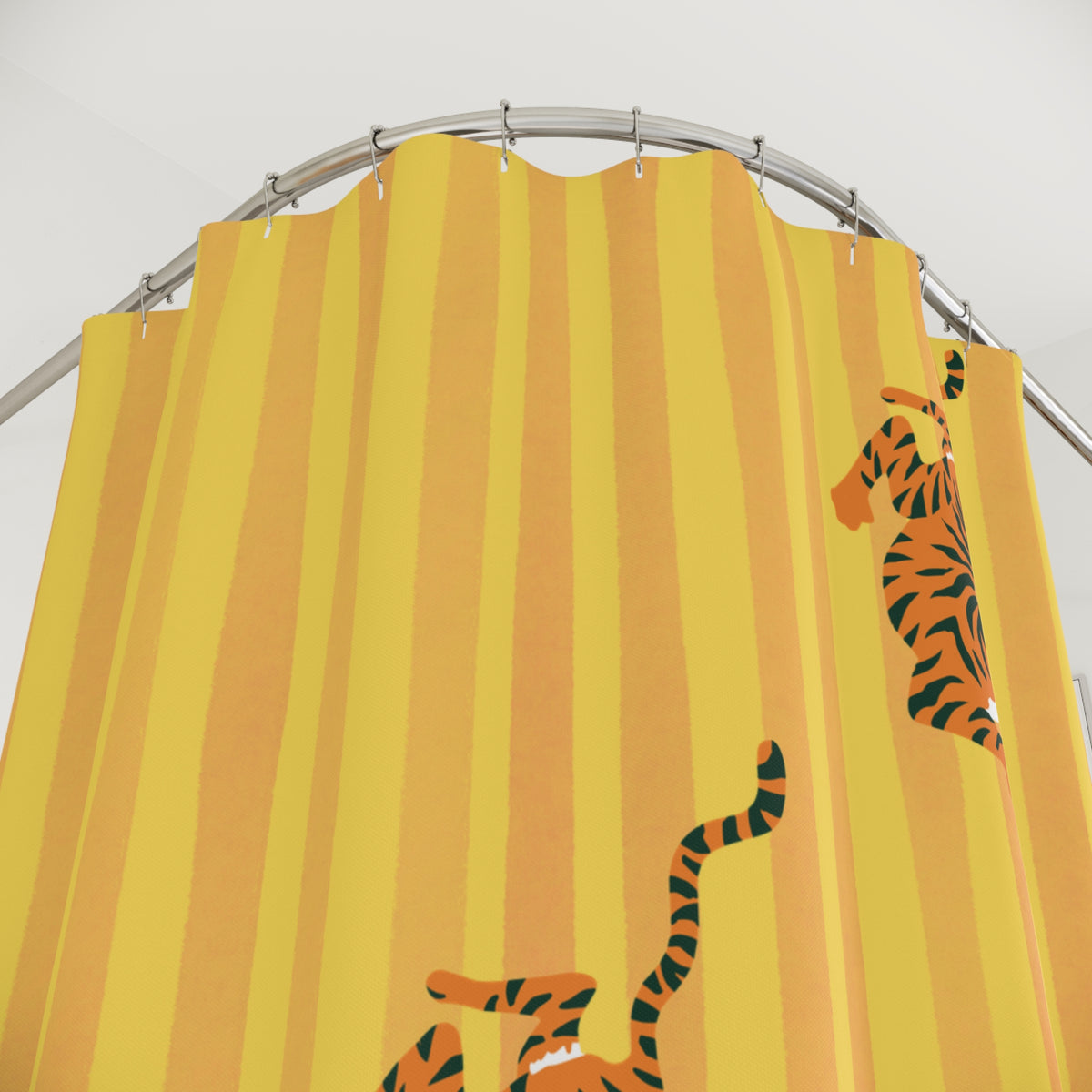 A yellow and orange striped shower curtain featuring cartoon tigers, hanging from a curved silver metal rod against a white wall.