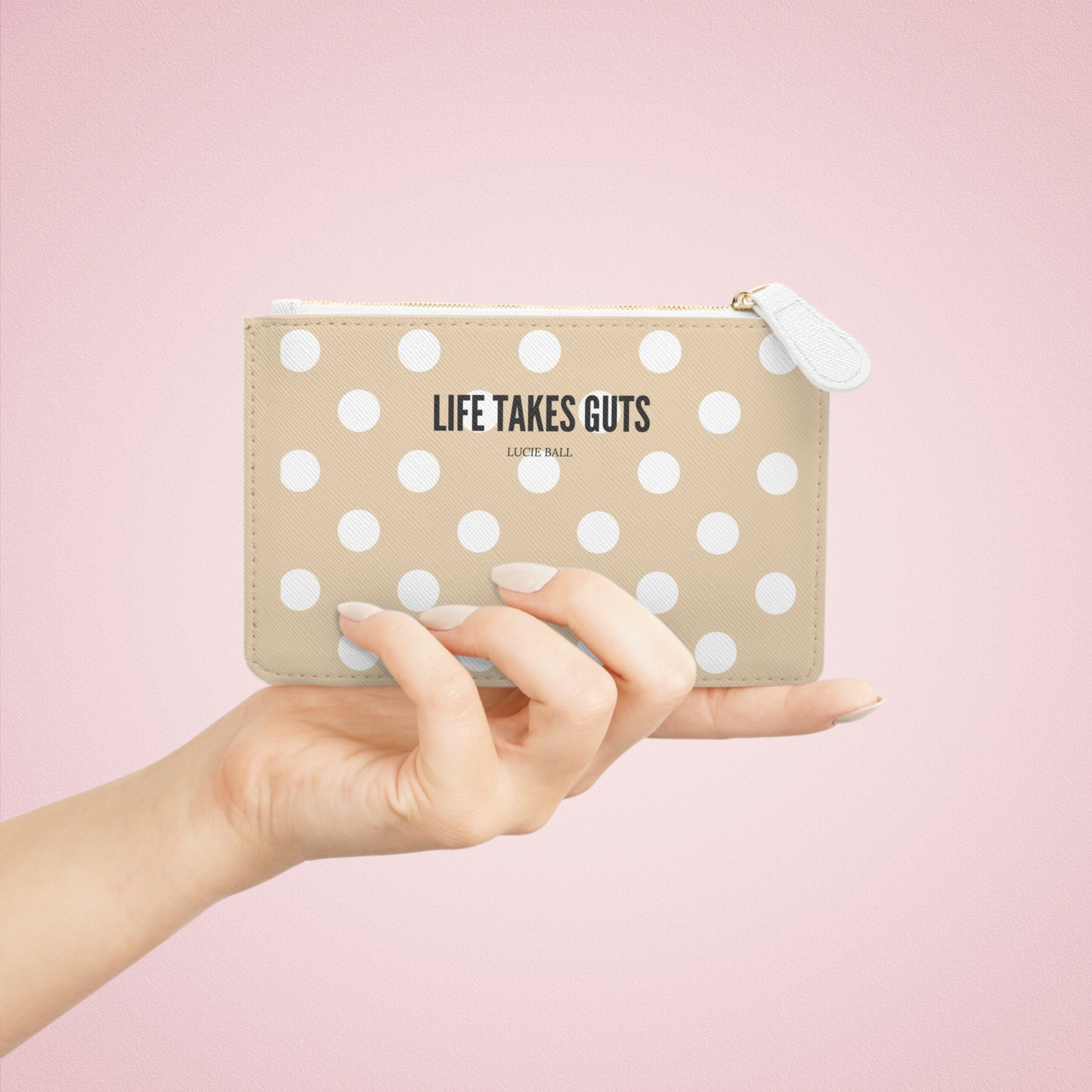 Hand holding a beige polka dot pouch with 'Life Takes Guts' text on a pink background