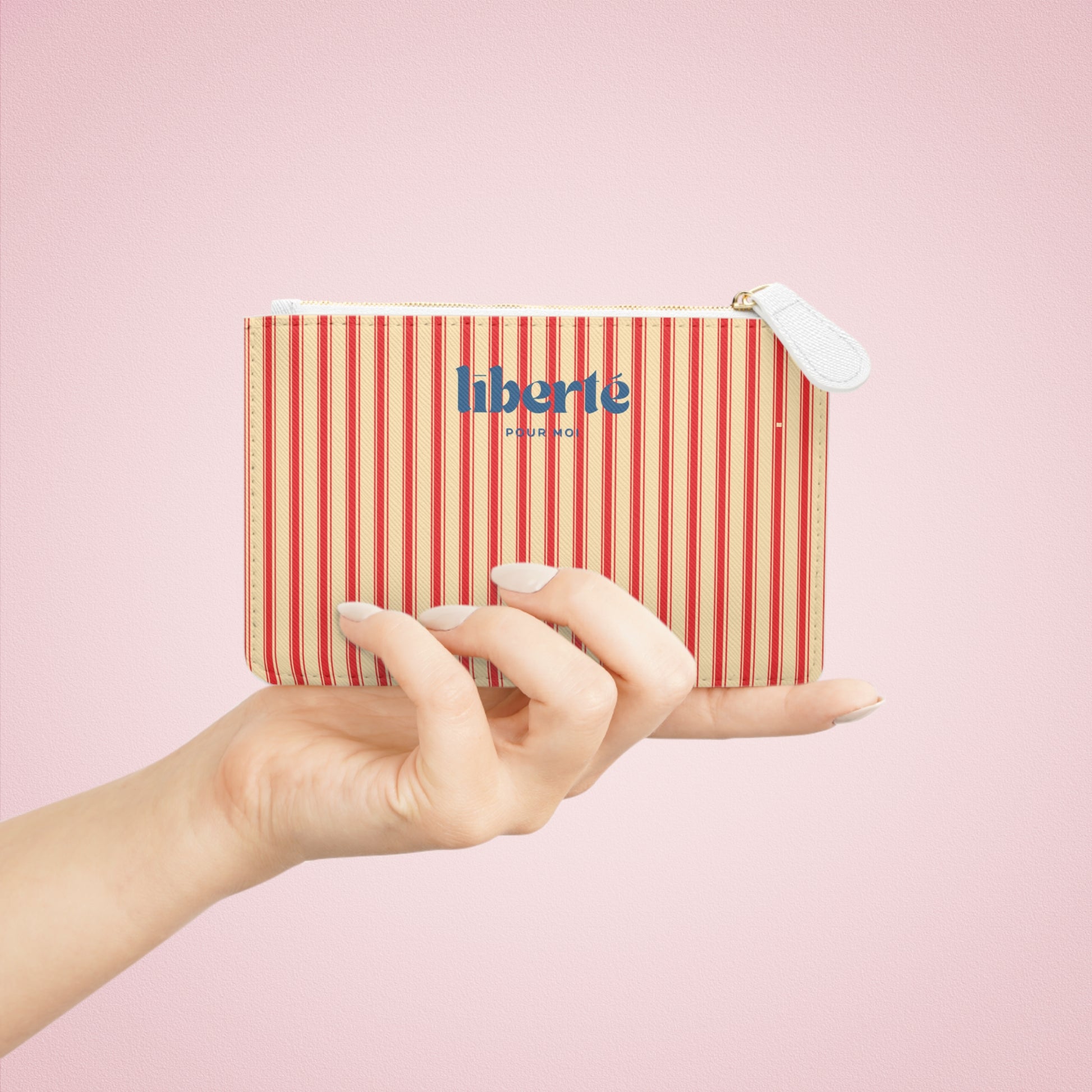 Hand holding a striped pouch with 'liberte' branding on a pink background
