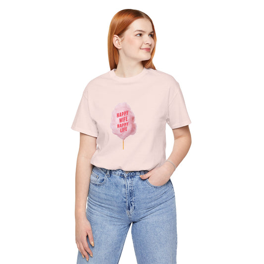 A woman with red hair wearing a light pink t-shirt with a pink cotton candy graphic that reads 'HAPPY WIFE HAPPY LIFE' and blue jeans, standing against a plain white background.