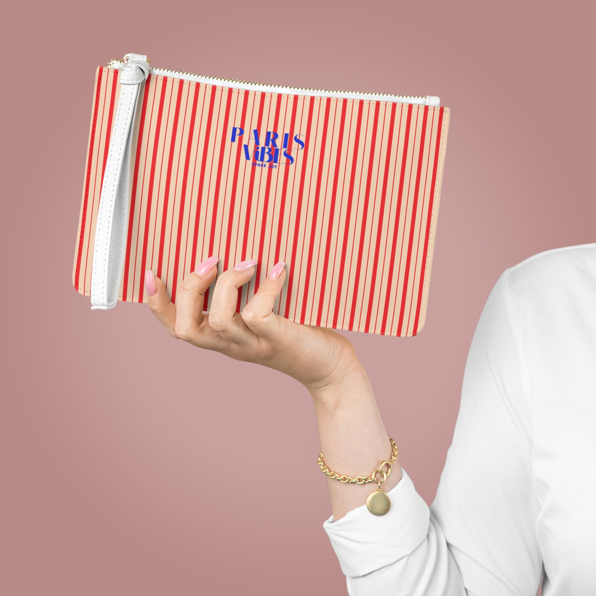 Hand holding a red and white striped pouch with 'Paris' text against a pink background