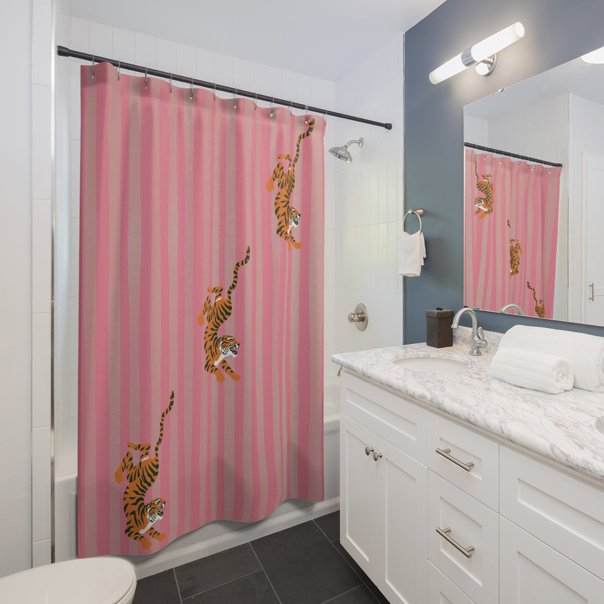 A pink striped shower curtain with orange and black tiger prints hanging in a modern white bathroom with a marble vanity and dark gray tile floor.