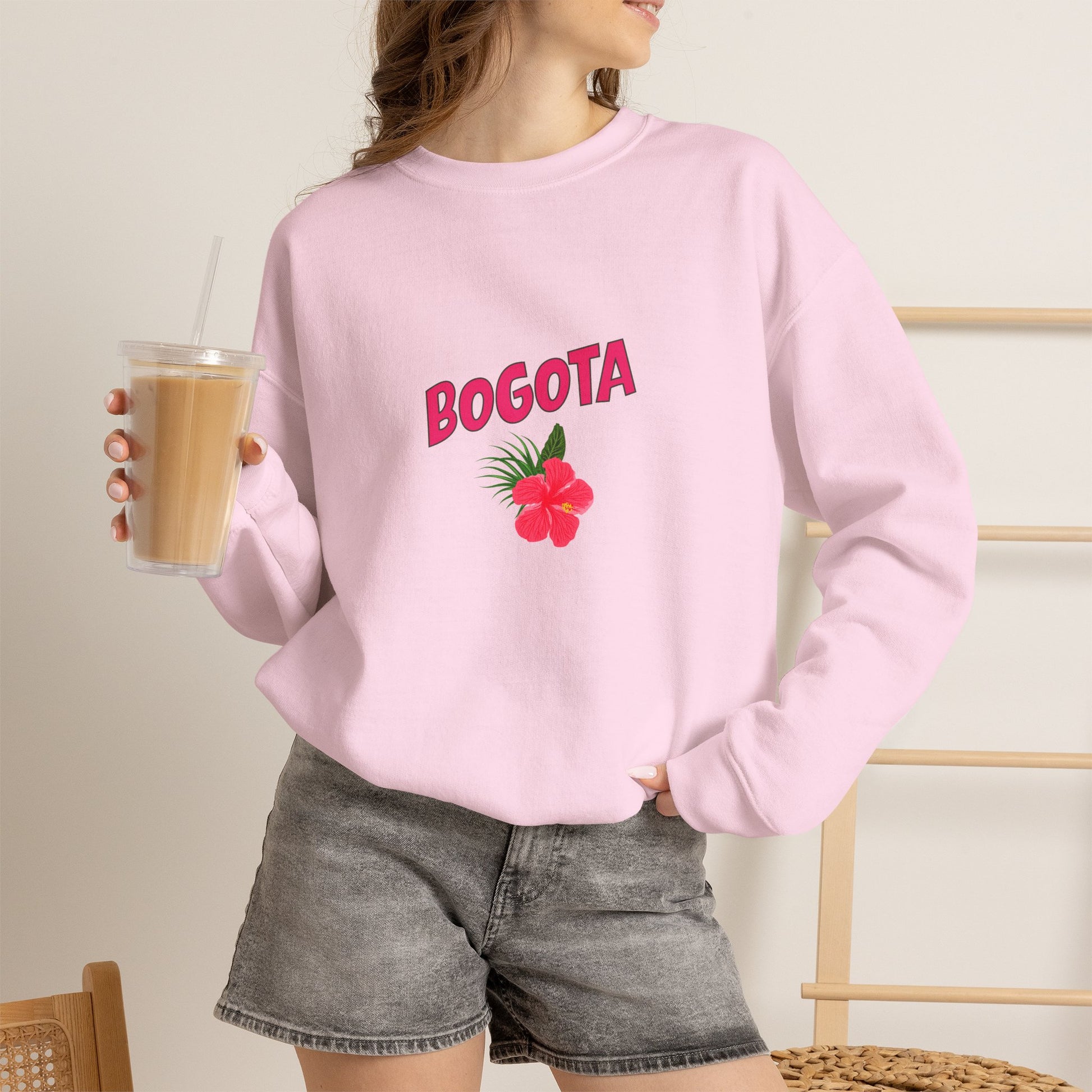 Person wearing a pink sweatshirt with 'BOGOTA' and a flower design, holding a drink.