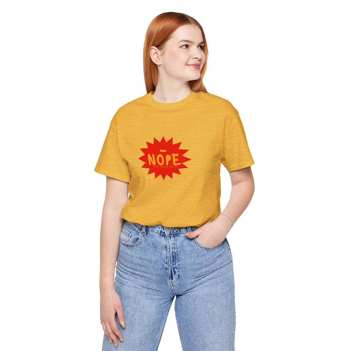 A woman with red hair wearing a heathered mustard yellow t-shirt with a red starburst graphic that says 'NOPE' in yellow, paired with light wash blue jeans, against a plain white background.