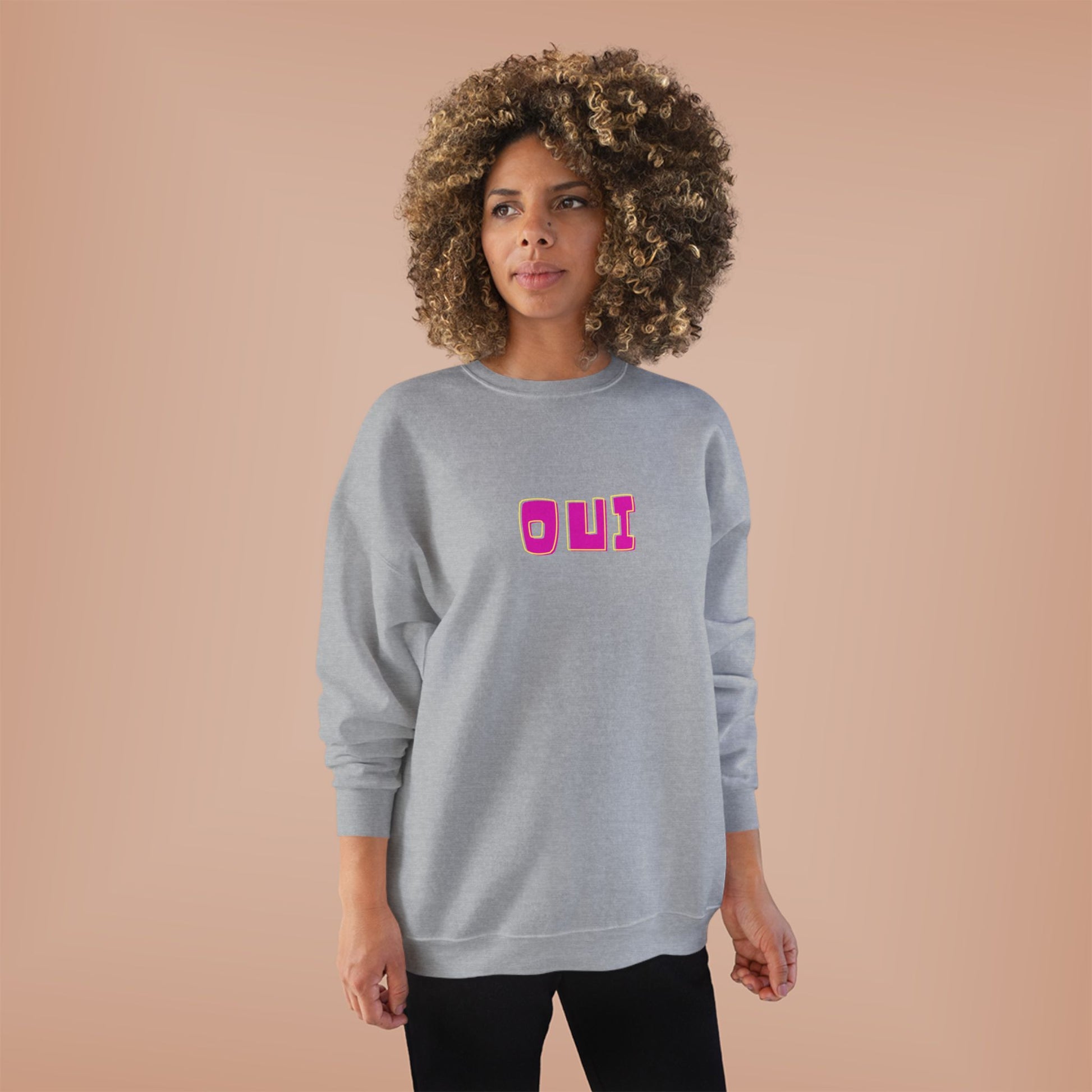 Woman wearing a gray sweatshirt with 'OUI' in pink on a beige background