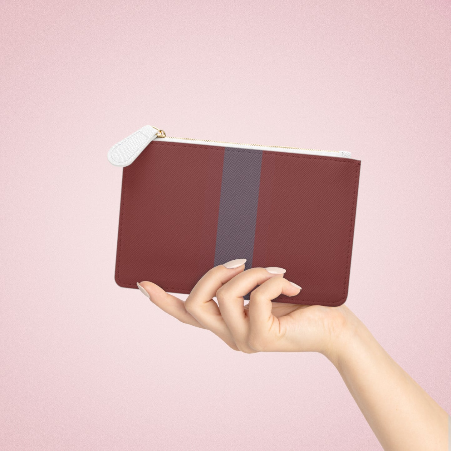 Hand holding a maroon pouch with a gray stripe against a pink background