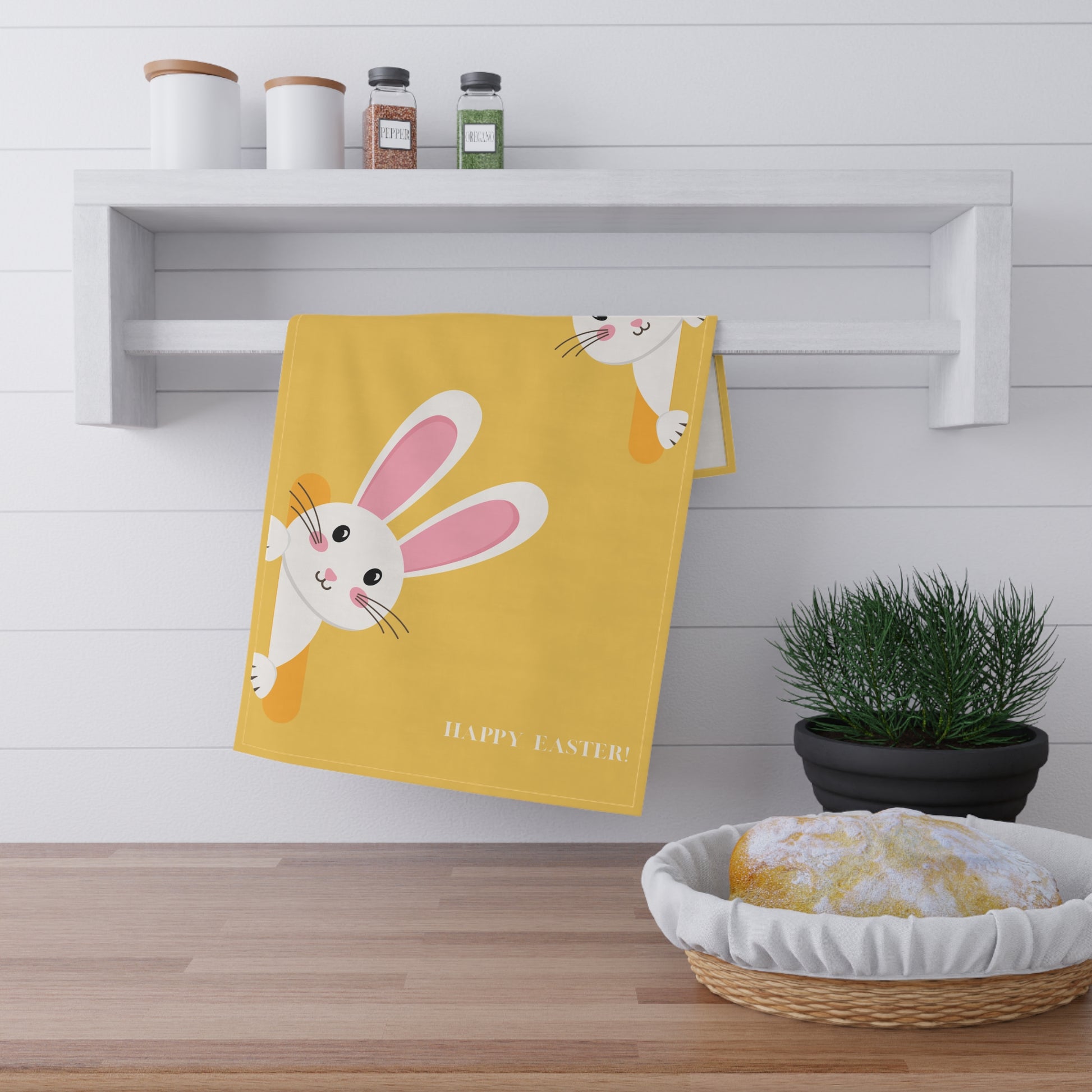 Yellow towel with bunny design and 'Happy Easter!' text hanging on a white wall above a wooden shelf.