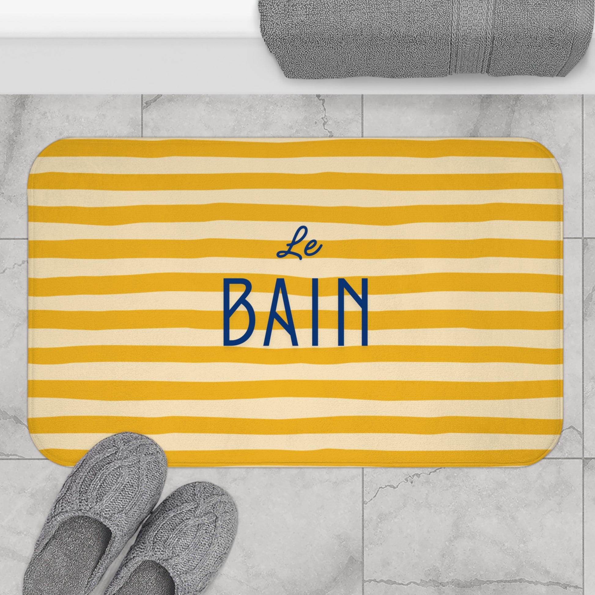 Yellow striped bath mat with 'Le Bain' text on a marble floor.