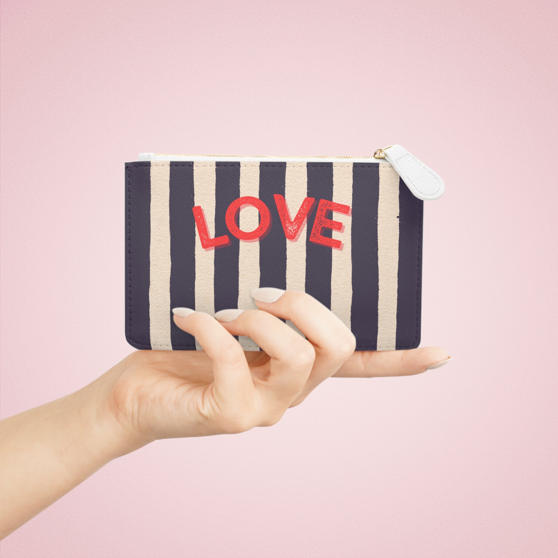 Striped pouch with 'LOVE' text held by a hand against a pink background