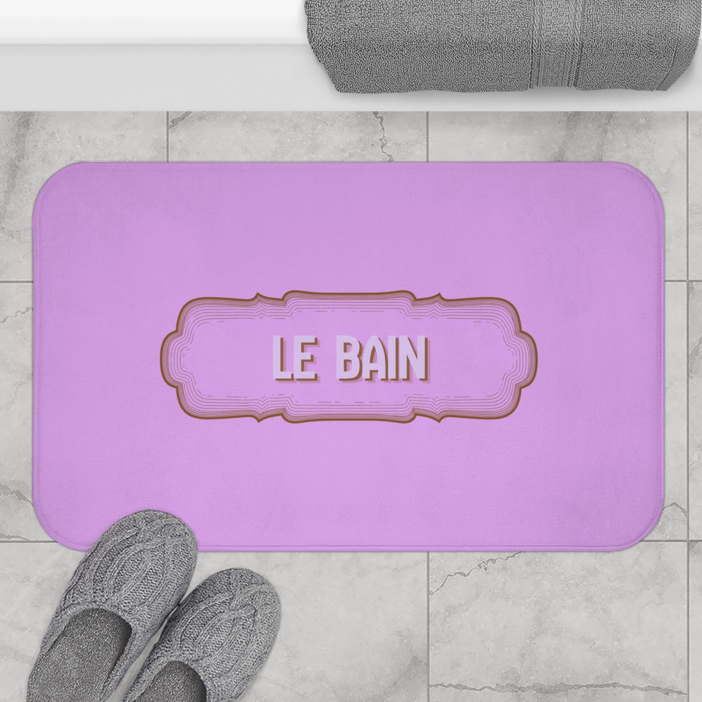 Purple bath mat with 'LE BAIN' text on a marble floor with gray slippers and towel.