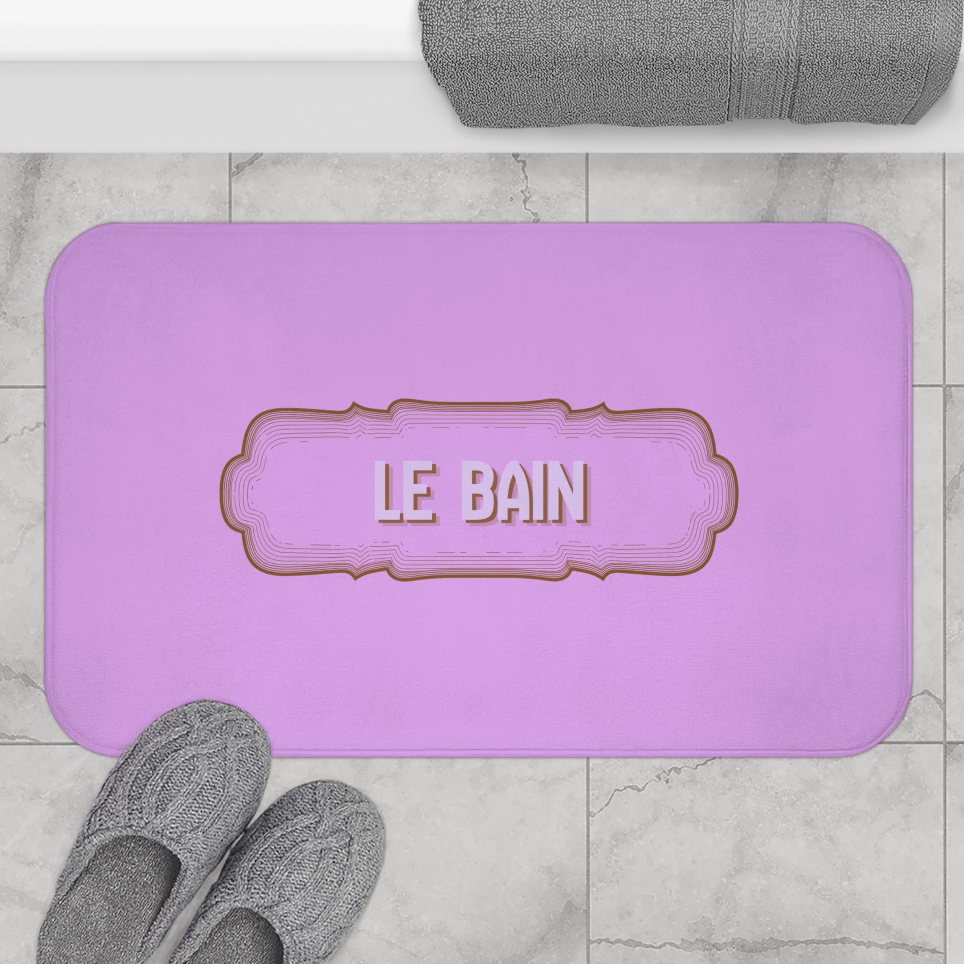 Purple bath mat with 'LE BAIN' text on a marble floor with gray slippers and towel.