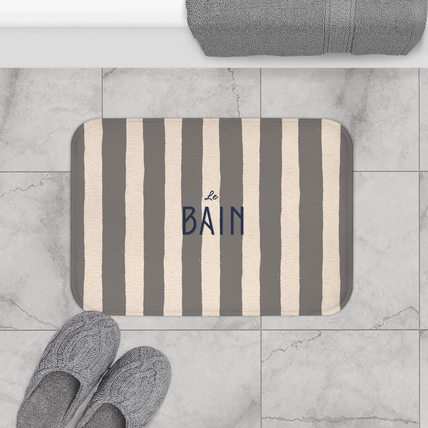 Striped bath mat with 'Le Bain' text on a tiled bathroom floor.