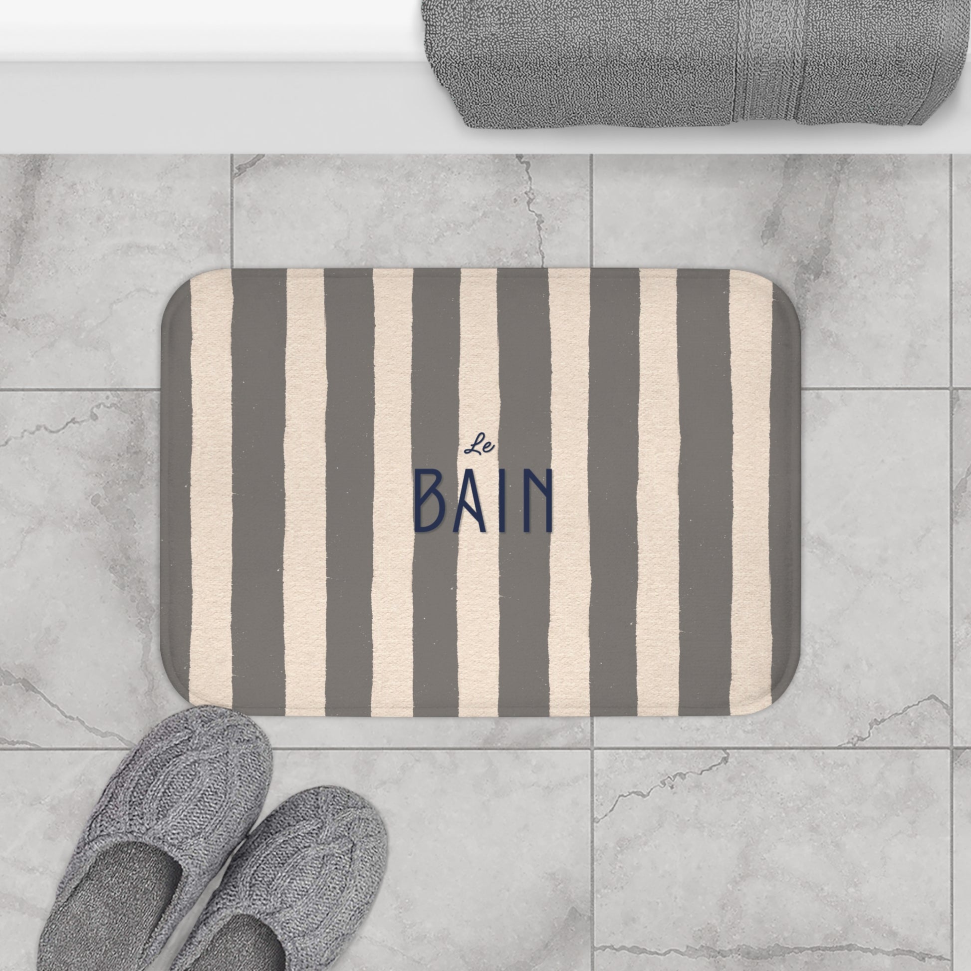 Striped bath mat with 'Le Bain' text on a tiled bathroom floor.
