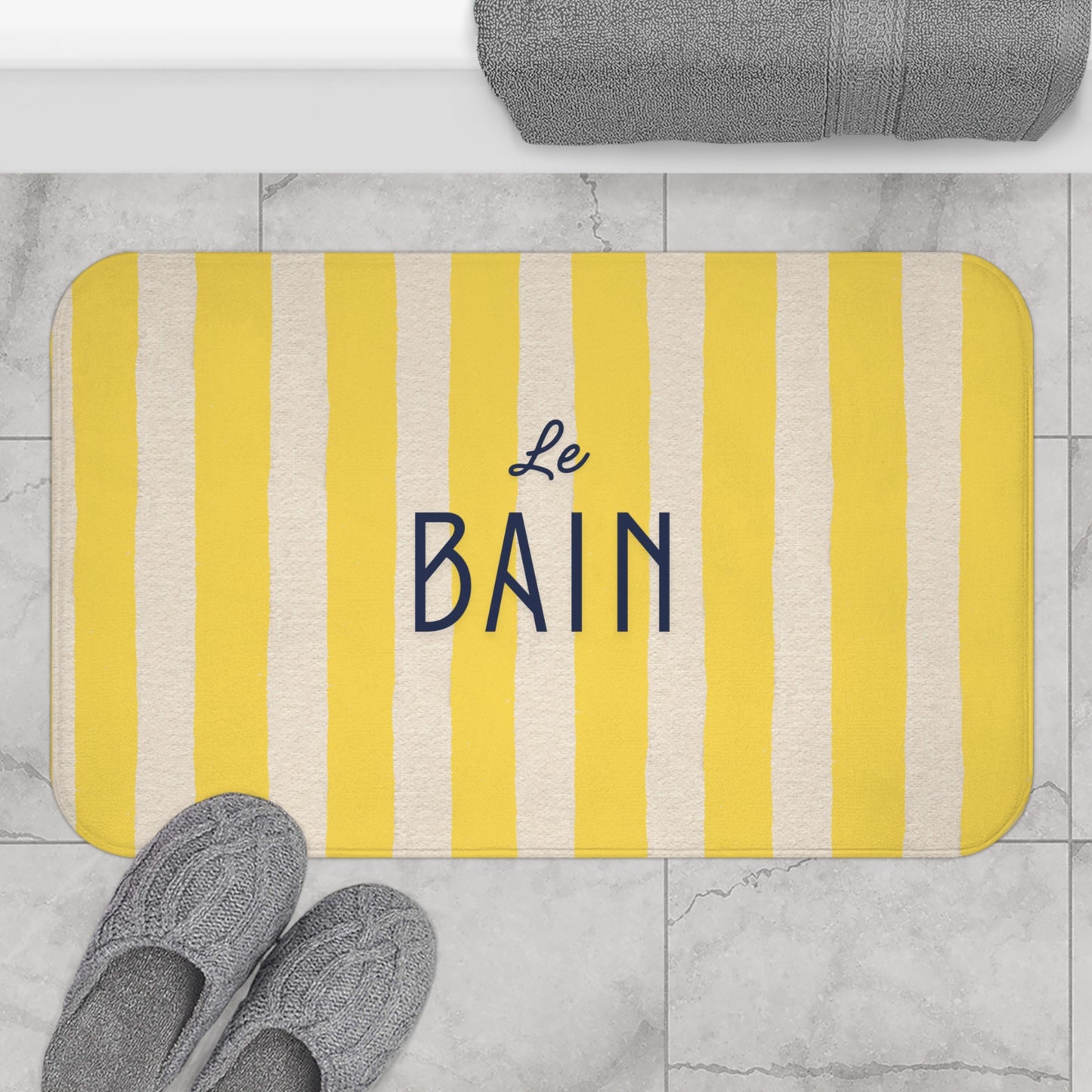 Yellow and white striped bath mat with 'Le Bain' text on a bathroom floor.