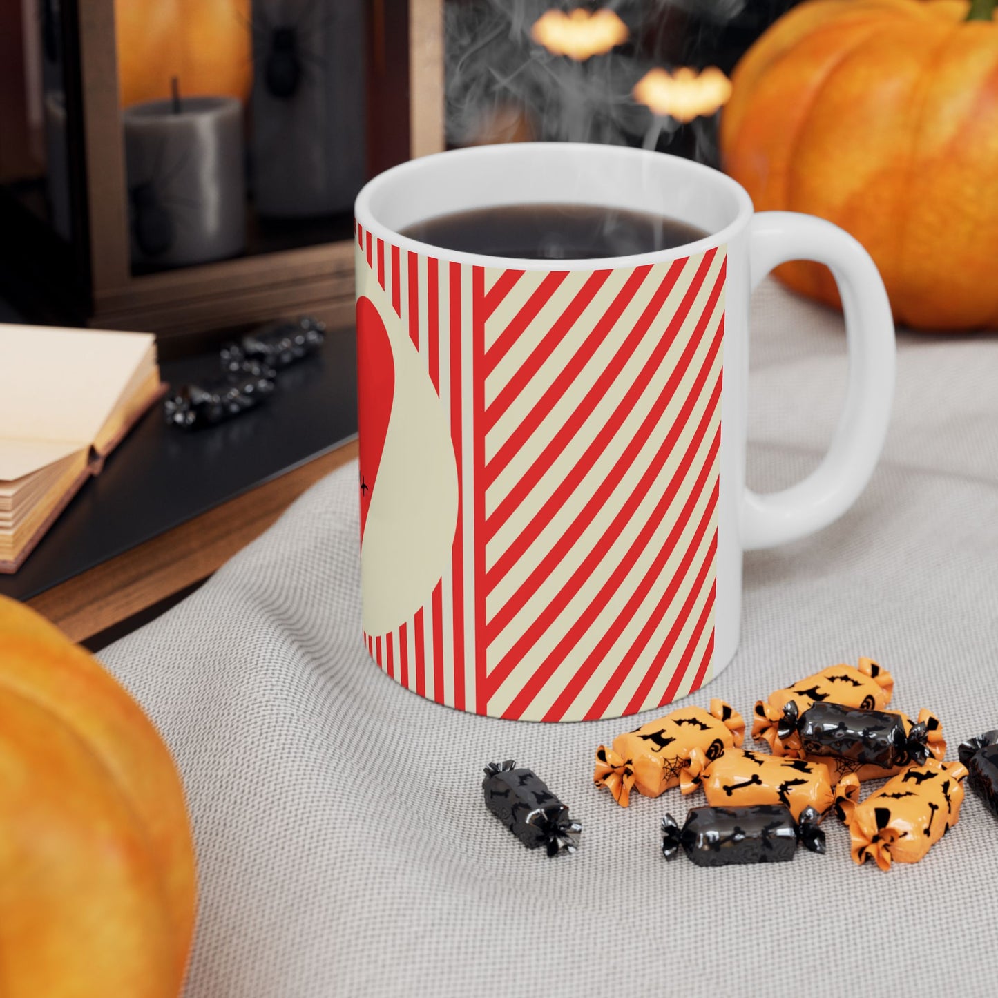 White mug with red and white striped design on a table with Halloween-themed treats and pumpkins.