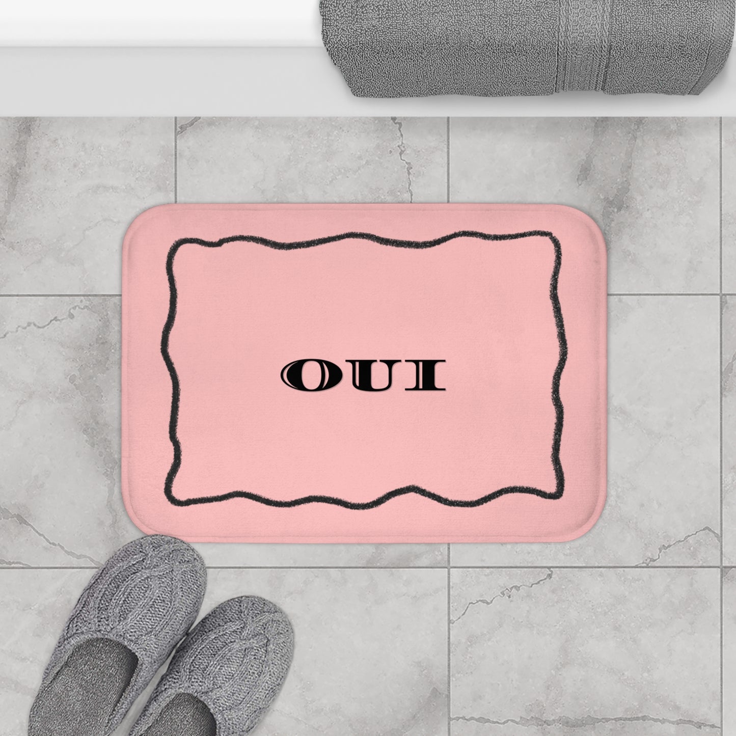 Pink bath mat with 'OUI' text on a tiled bathroom floor.