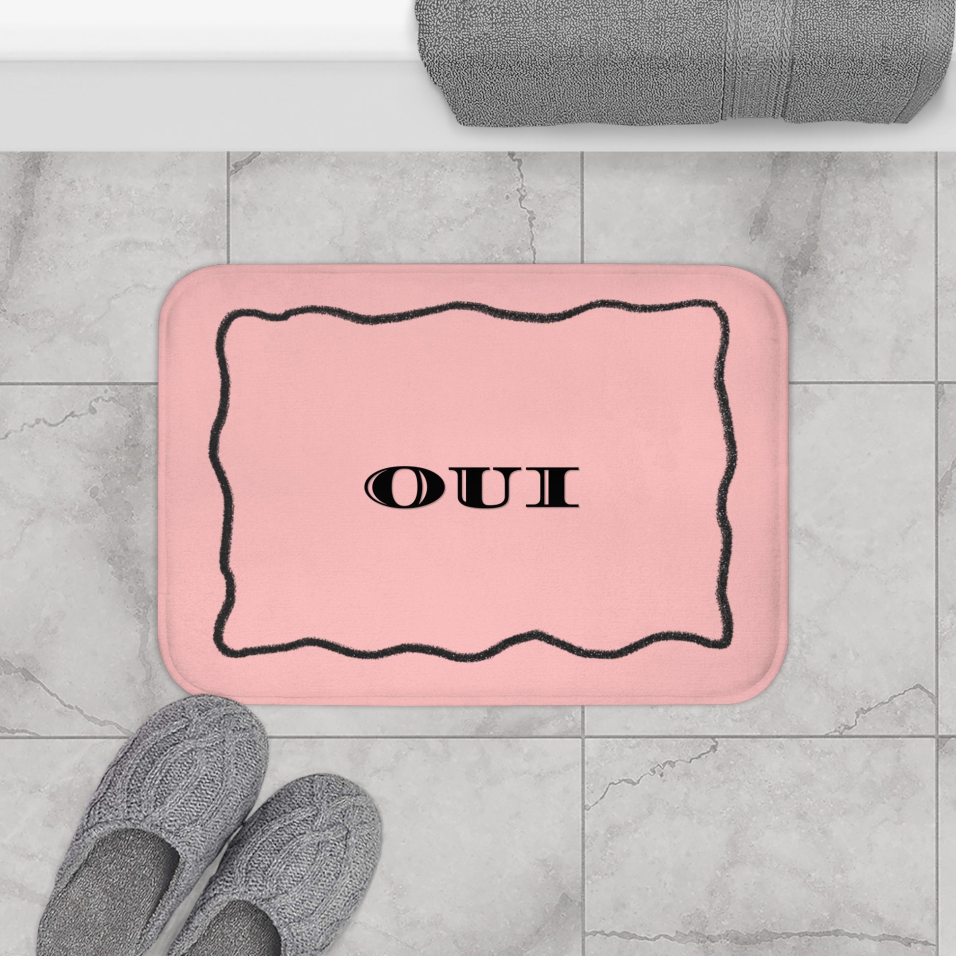 Pink bath mat with 'OUI' text on a tiled bathroom floor.