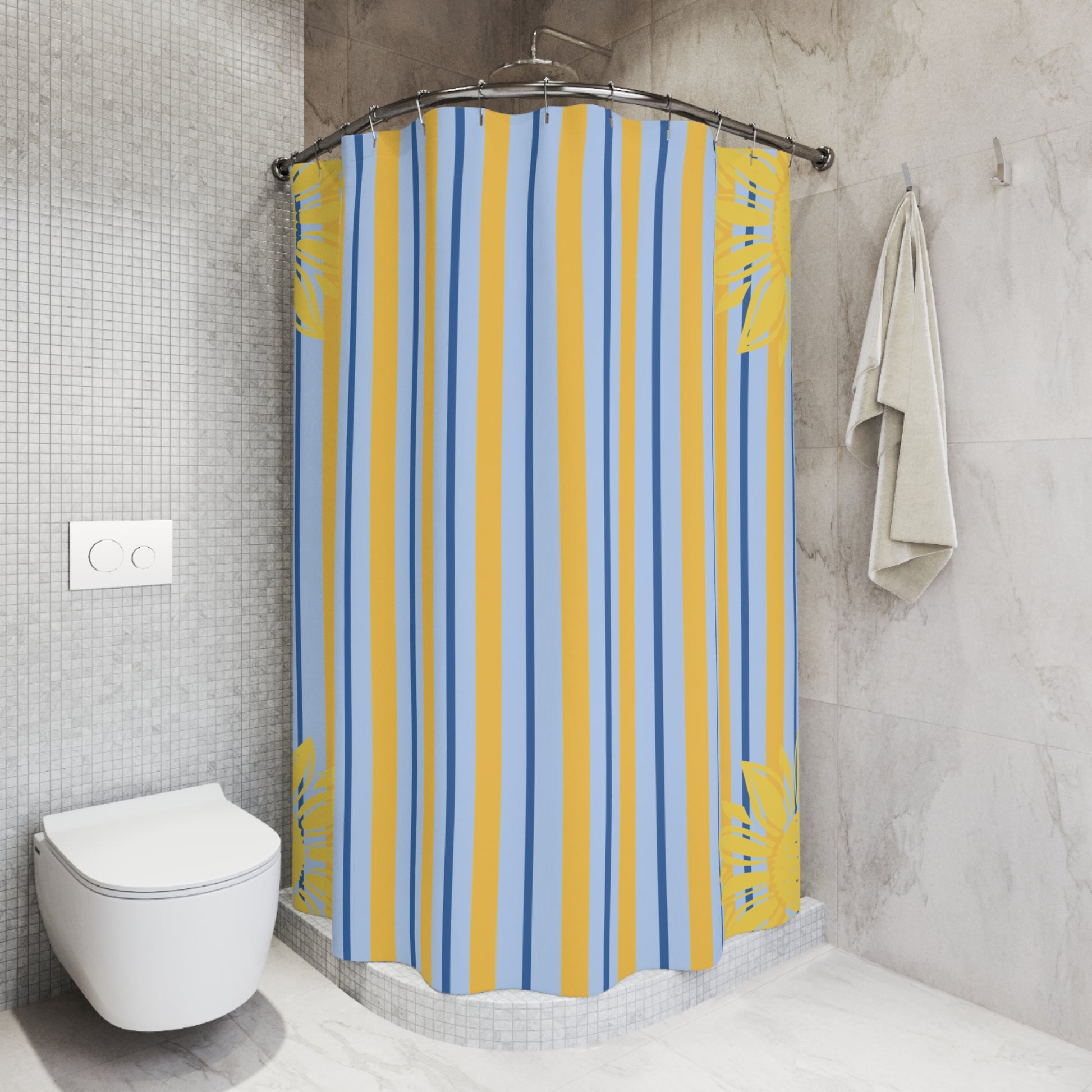 A shower curtain with vertical blue and yellow stripes and tropical leaf motifs, hanging in a modern tiled bathroom next to a toilet and a hanging towel.