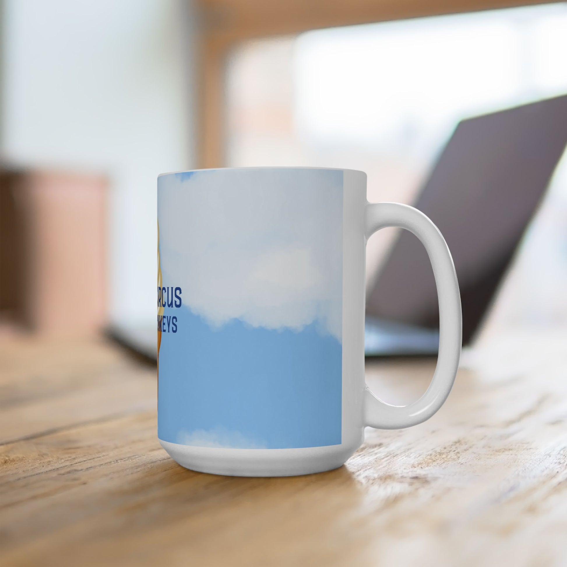 A white ceramic coffee mug with a blue sky and clouds print, sitting on a wooden table with a blurred laptop in the background.