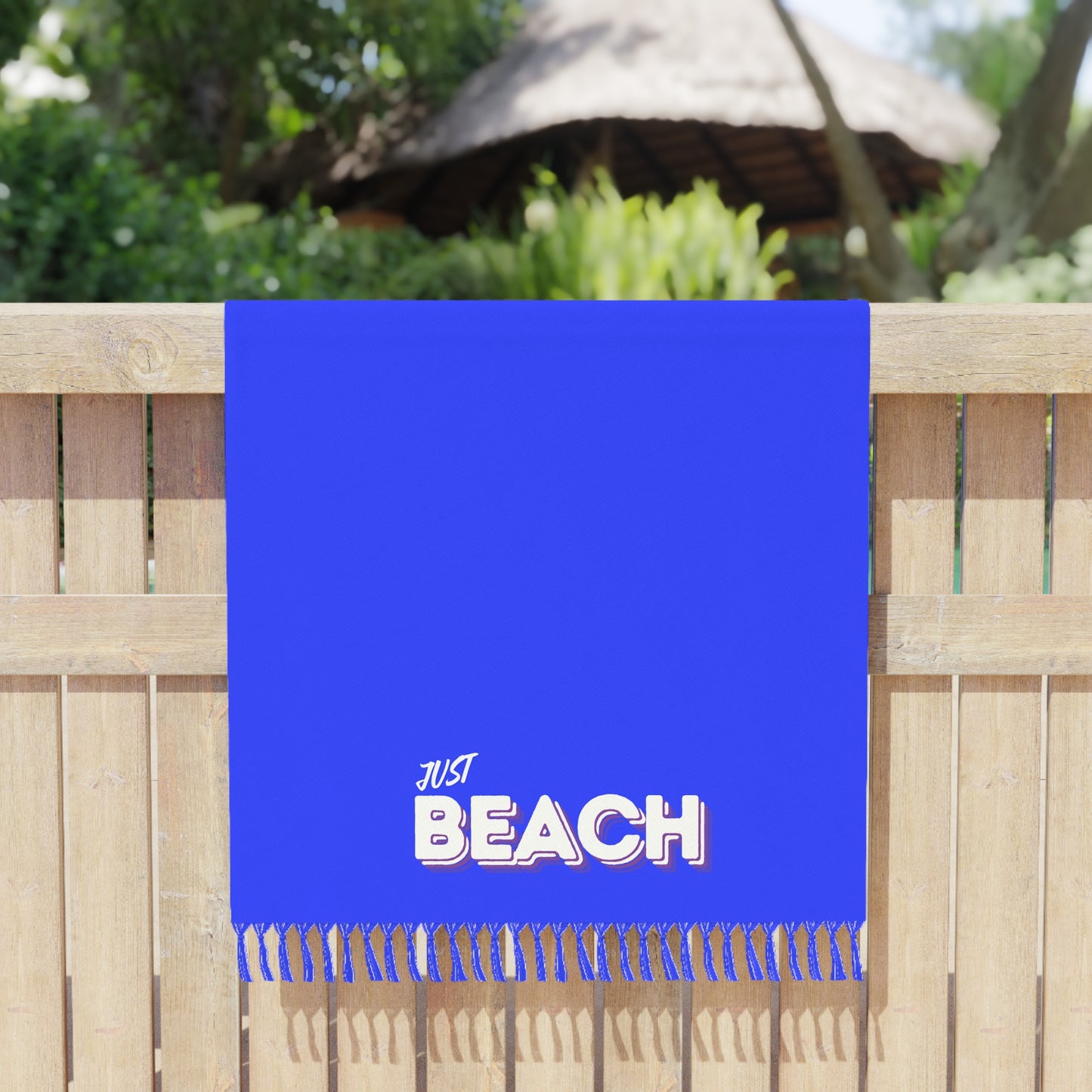 Blue beach towel with 'JUST BEACH' text on a wooden fence