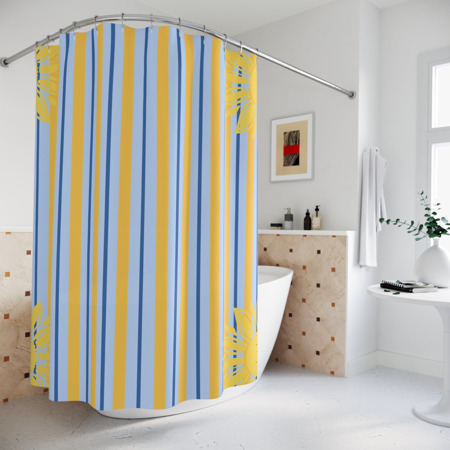 A shower curtain with vertical stripes in blue, yellow, and white, featuring yellow tropical leaf patterns at the corners, hanging in a bright white bathroom.
